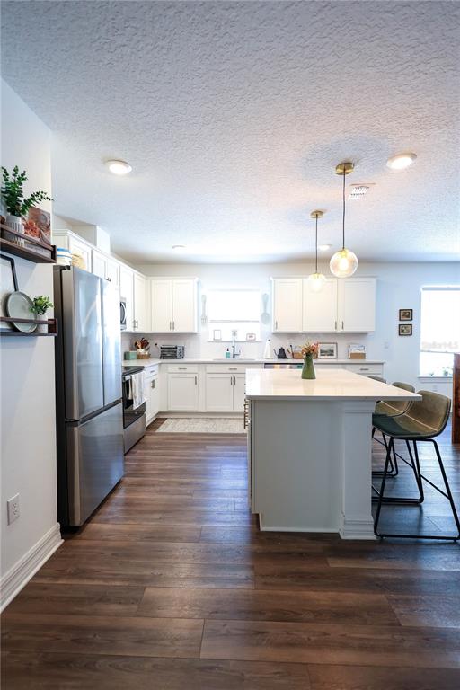 A modern kitchen features white cabinetry, a central island with bar seating, and wood-look flooring — 9553 SUMMERS CAY CIRCLE, THONOTOSASSA, FL