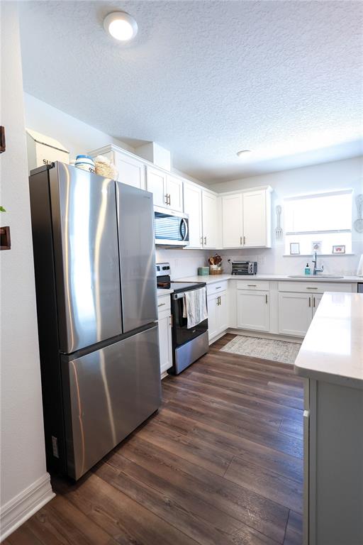 A kitchen features white cabinetry, stainless steel appliances, and wood-look flooring — 9553 SUMMERS CAY CIRCLE, THONOTOSASSA, FL