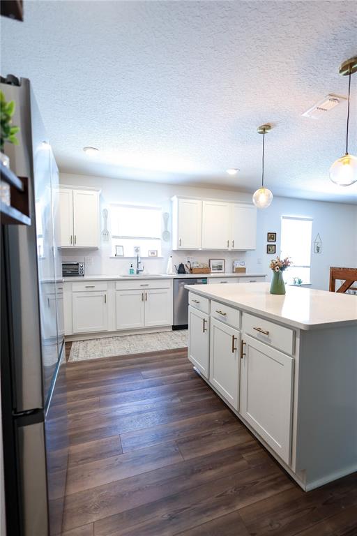 A kitchen features white cabinetry, a central island with a countertop, and dark wood flooring — 9553 SUMMERS CAY CIRCLE, THONOTOSASSA, FL