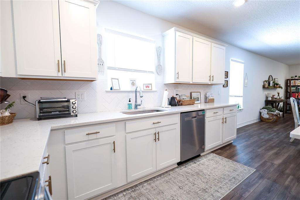 A kitchen features white cabinets, light countertops, a stainless steel dishwasher, and dark wood flooring — 9553 SUMMERS CAY CIRCLE, THONOTOSASSA, FL
