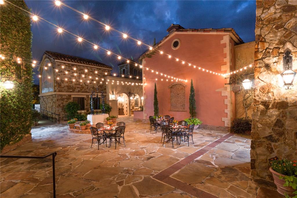 An outdoor stone patio features dining tables, string lights, and Mediterranean-style buildings at dusk — 15381 APENNINE WAY, MONTVERDE, FL