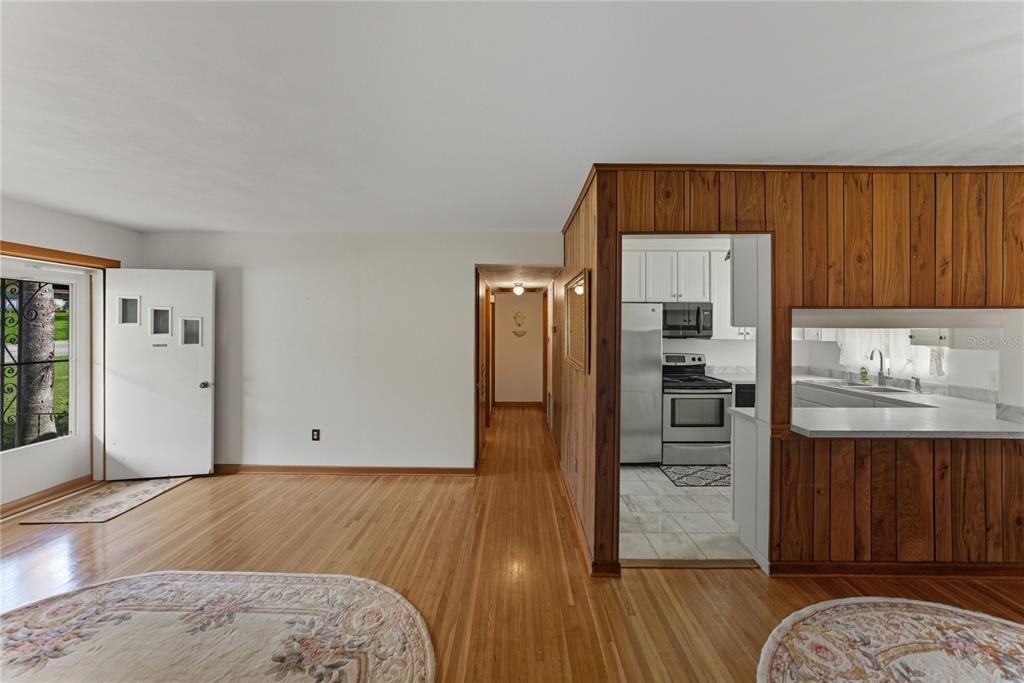 A living room with hardwood floors leads to a hallway and a wood-paneled kitchen — 307 GLENDALE ST, LAKELAND, FL