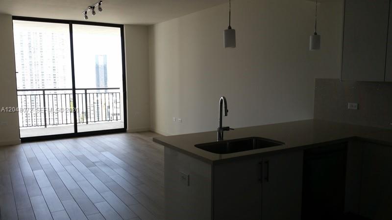 A modern kitchen island with a sink overlooks an open living area with balcony access — 999 SW 1st Ave # 2510, Miami FL 33130, MIAMI, FL