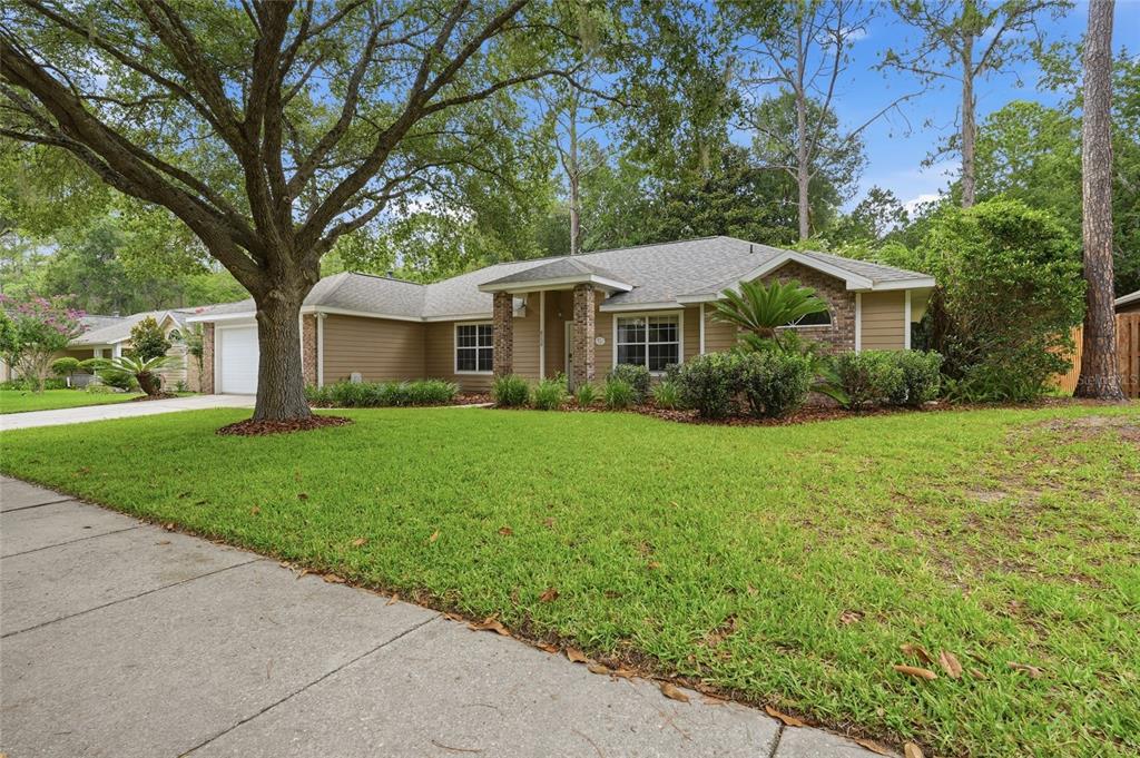 A single-story house with tan siding, a brick entryway, and a large tree in front — 8158 SW 51ST BOULEVARD, GAINESVILLE, FL
