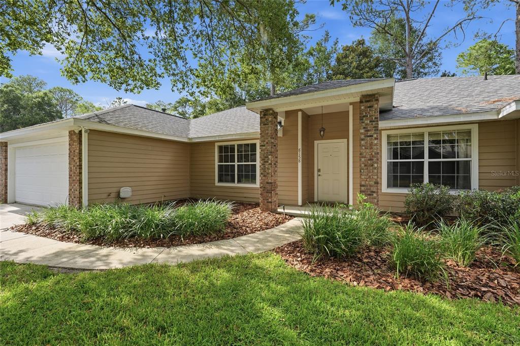 A single-story house with tan siding, a brick-columned entryway, and a white garage door — 8158 SW 51ST BOULEVARD, GAINESVILLE, FL