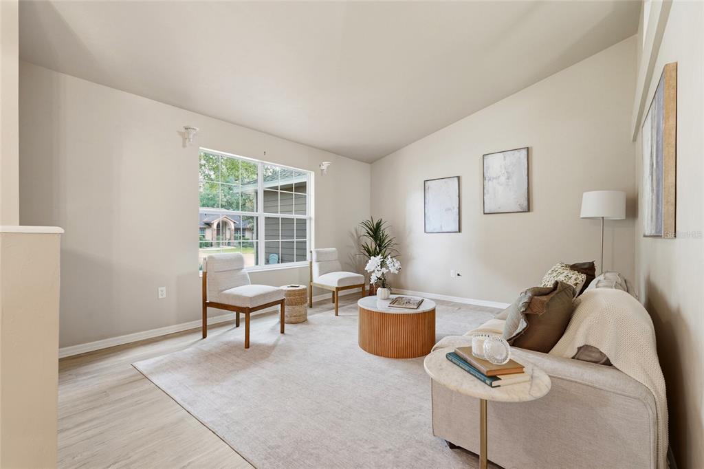 A living room features light-colored walls, wood-look flooring, a large window, and neutral furniture — 8158 SW 51ST BOULEVARD, GAINESVILLE, FL