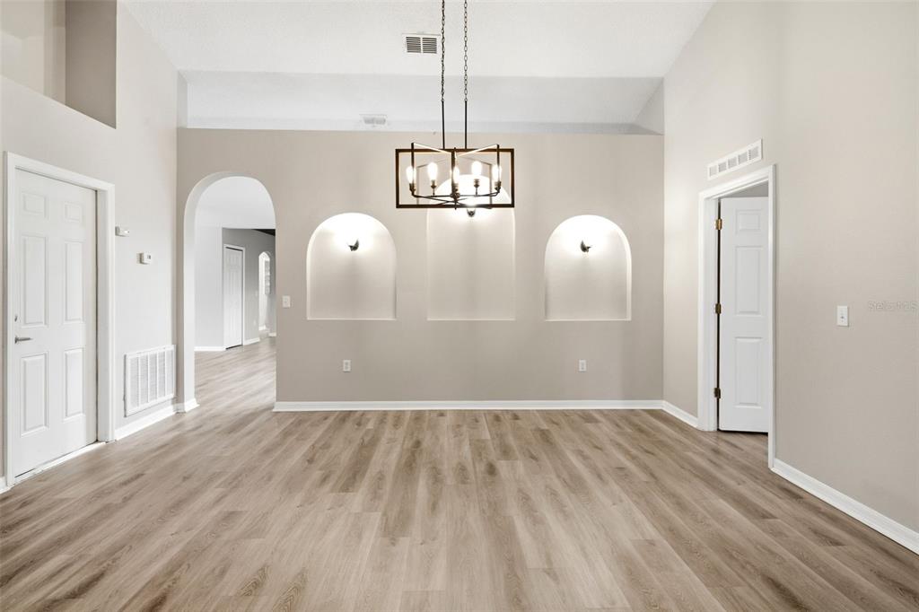A living room with light gray walls, wood-look flooring, vaulted ceilings, and three arched niches — 134 CROWN COLONY WAY, SANFORD, FL