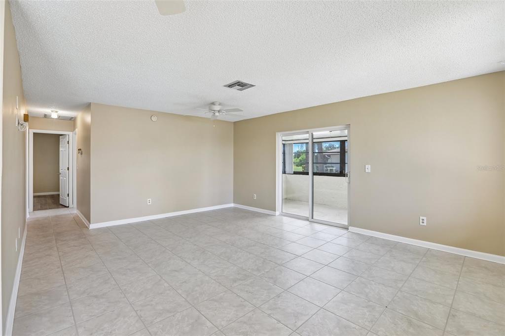 An empty living room features beige walls, light-colored tile flooring, and a sliding glass door — 1418 14TH CIRCLE SE, LARGO, FL