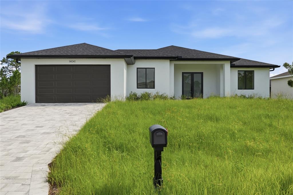 A modern, white single-story house with a dark roof, garage, and tall, unkempt grass — 14041 NEWSON LANE, PORT CHARLOTTE, FL