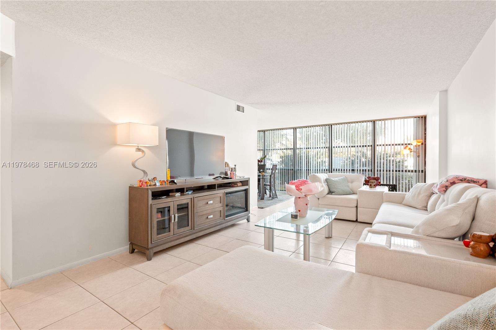A living room features tile flooring, a large sectional sofa, and a television console — 1000 Parkview Dr # 115, Hallandale Beach FL 33009, HALLANDALE BEACH, FL