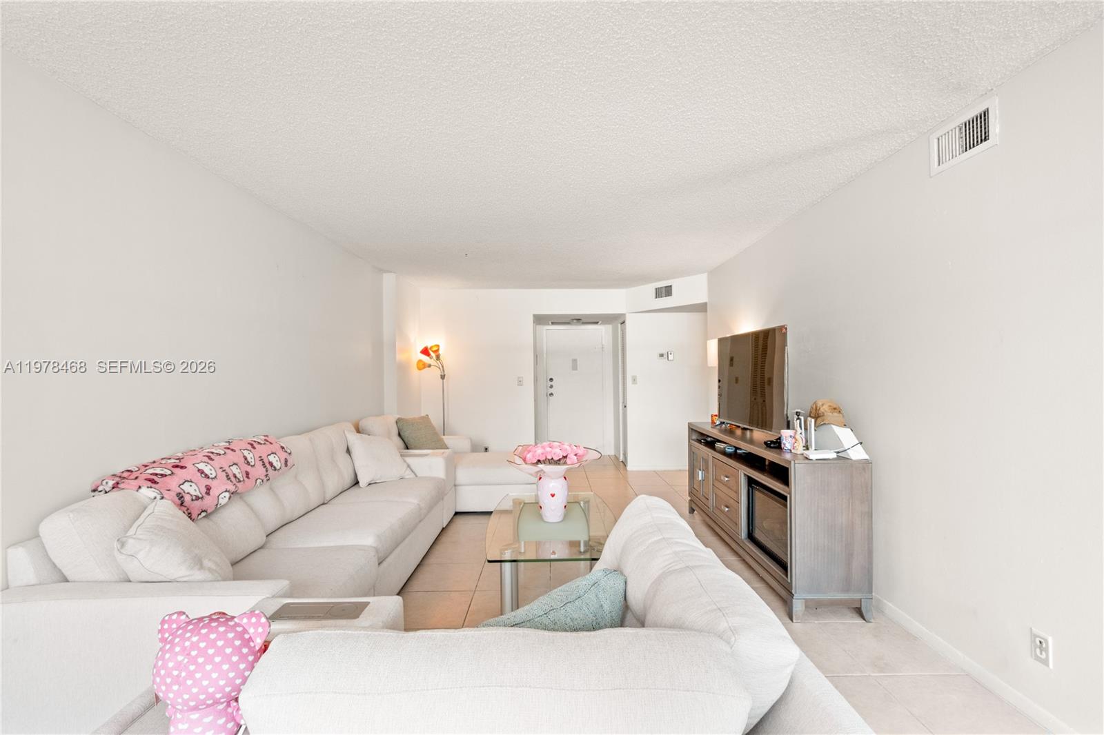 A living room features a large sectional sofa, a glass coffee table, and a television console — 1000 Parkview Dr # 115, Hallandale Beach FL 33009, HALLANDALE BEACH, FL