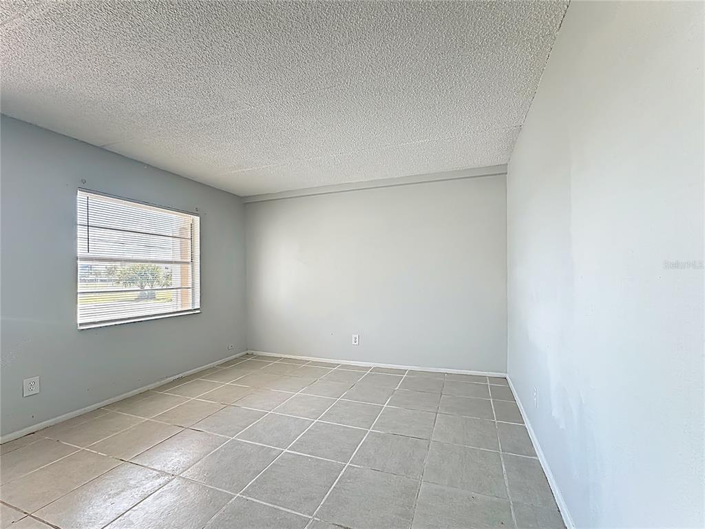 An empty room features light gray walls, a textured ceiling, and large square floor tiles — 694 MICHIGAN COURT UNIT 4, ST CLOUD, FL