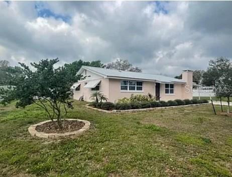 A light pink, single-story house with a metal roof sits on a grassy lot — 1305 CARR DRIVE, AUBURNDALE, FL