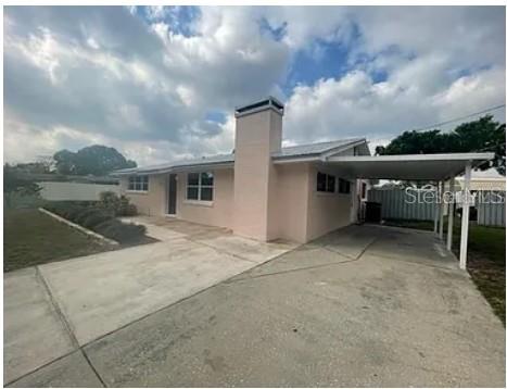 A single-story pink house with a chimney and an attached carport under a cloudy sky — 1305 CARR DRIVE, AUBURNDALE, FL