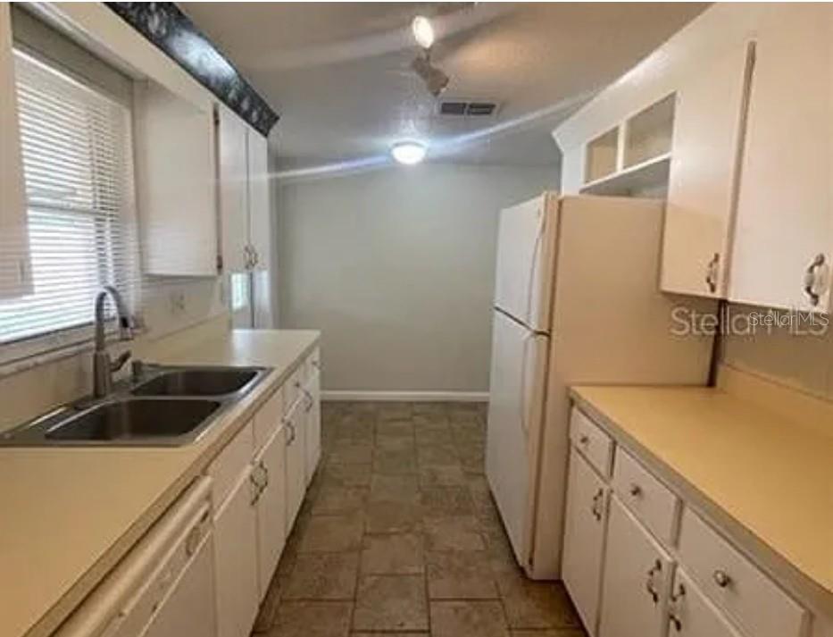 A galley kitchen features white cabinets, laminate countertops, a double sink, and white appliances — 1305 CARR DRIVE, AUBURNDALE, FL