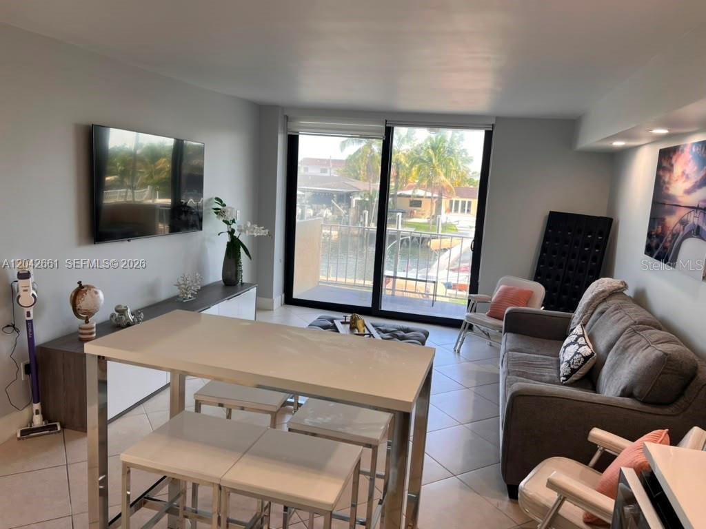 A living room features a grey sofa, a dining table, and sliding doors overlooking water — 2350 NE 135TH STREET UNIT 209, NORTH MIAMI, FL