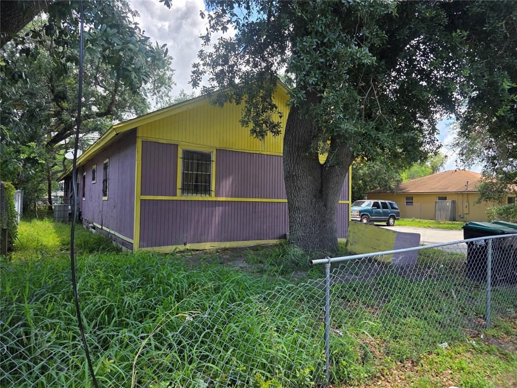 A purple and yellow house stands behind a chain-link fence near a large tree — 4429 CYPRESS STREET, ORLANDO, FL