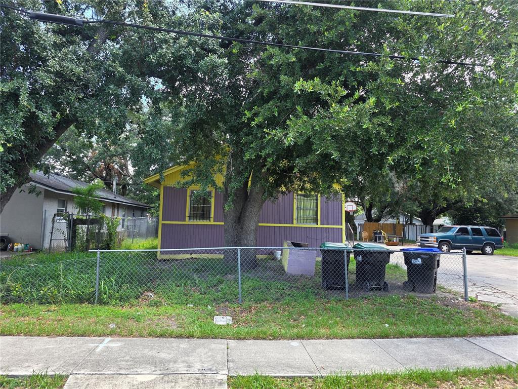 A yellow and purple house sits behind a chain-link fence under a large tree — 4429 CYPRESS STREET, ORLANDO, FL