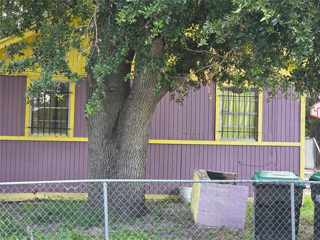 A large tree stands in front of a purple and yellow house with barred windows — 4429 CYPRESS STREET, ORLANDO, FL