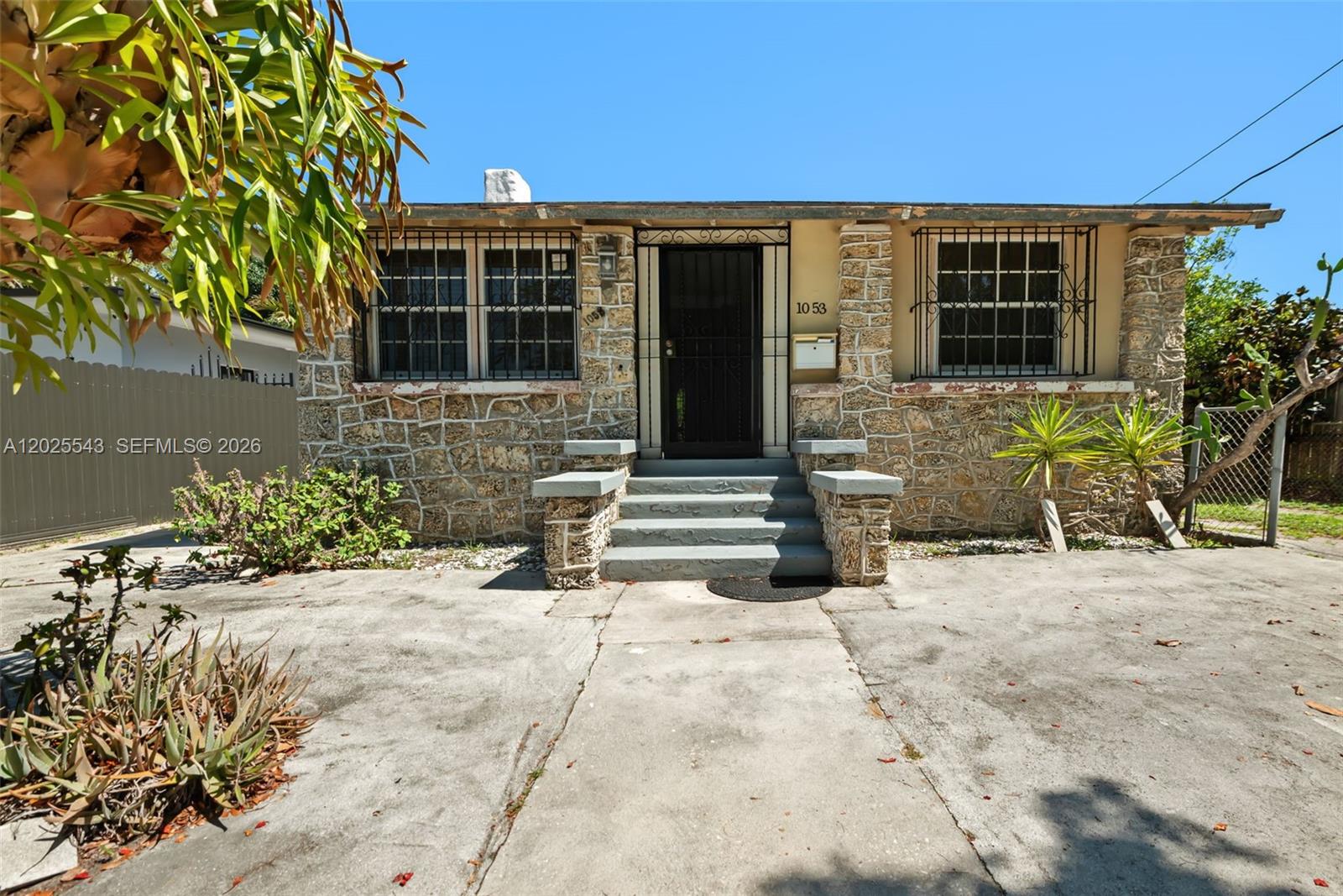 A single-story house features a stone facade, a central front door, and security window bars — 1053 NW 28th St, Miami FL 33127, MIAMI, FL