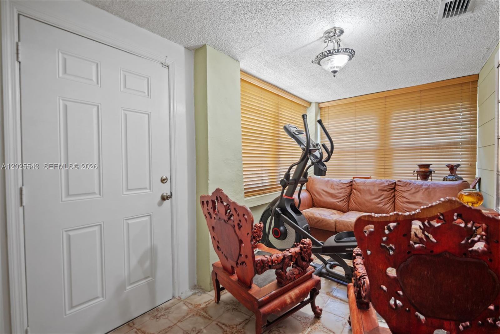 A room with a white door, tile flooring, an elliptical machine, and two ornate wooden chairs — 1053 NW 28th St, Miami FL 33127, MIAMI, FL