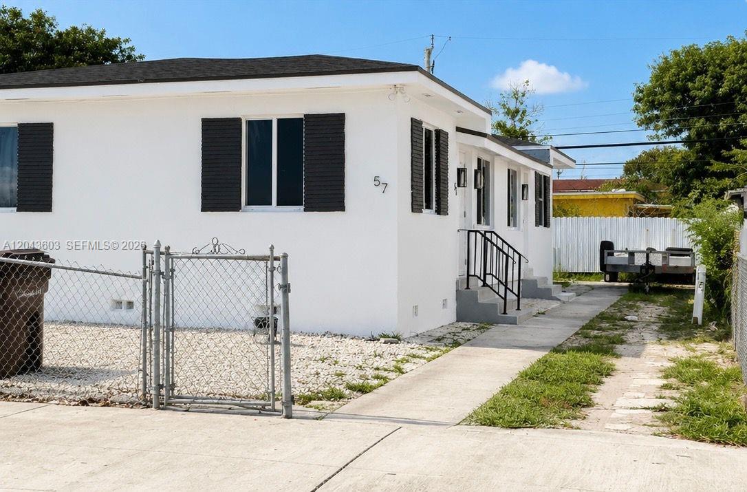 A white single-story house features black shutters, a chain-link fence, and a concrete driveway — 59 E 10th St, Hialeah FL 33010, HIALEAH, FL
