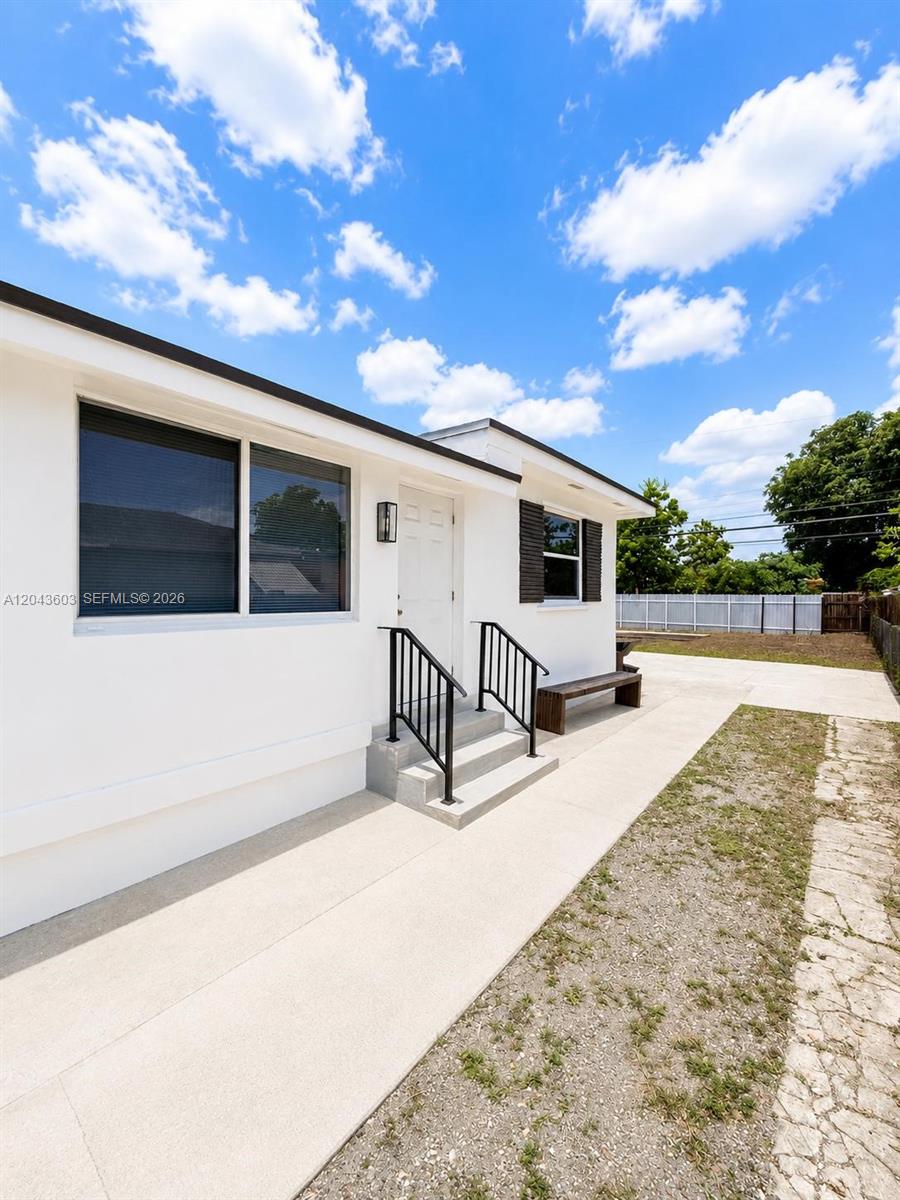 A white exterior wall features a doorway with black railings and a concrete walkway — 59 E 10th St, Hialeah FL 33010, HIALEAH, FL