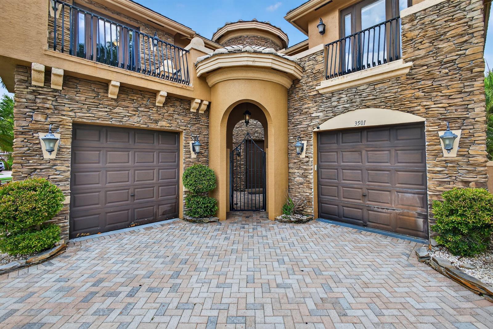 A two-story house exterior features stone siding, two garage doors, and a central gated entrance — 3501 Collonade Drive, Wellington FL 33449, WELLINGTON, FL