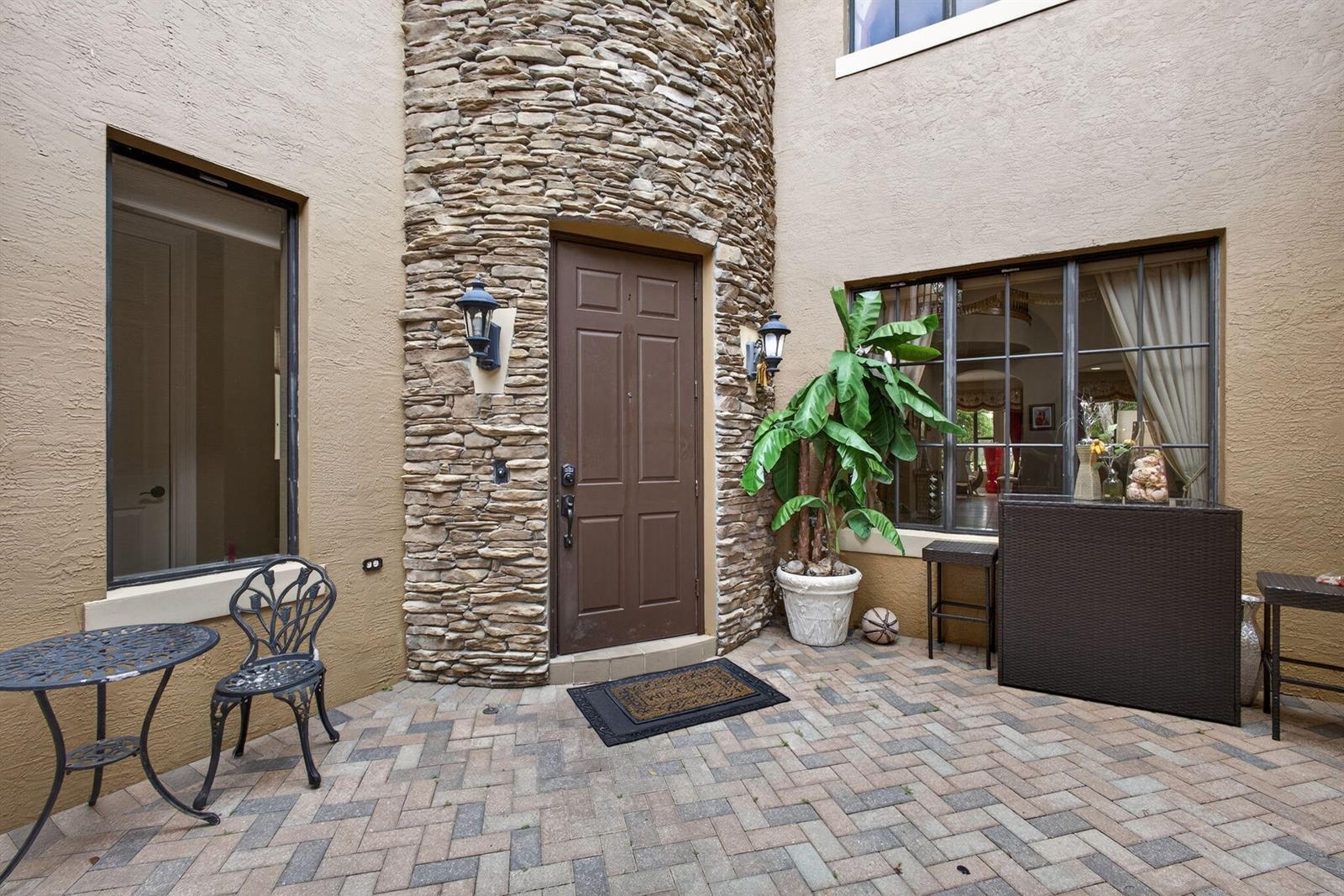 A stone-clad entryway features a brown door, a brick-paver patio, and a potted plant — 3501 Collonade Drive, Wellington FL 33449, WELLINGTON, FL