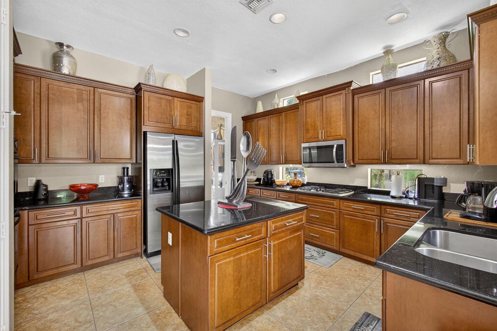 A kitchen with wood cabinets, black countertops, stainless steel appliances, and tile flooring — 3501 Collonade Drive, Wellington FL 33449, WELLINGTON, FL