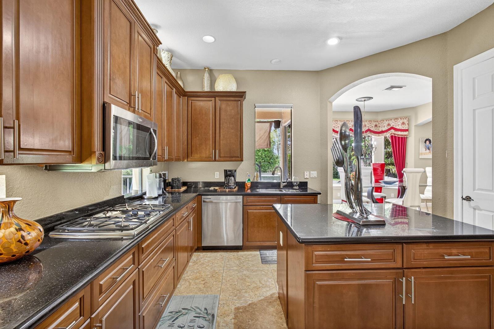 A kitchen features wood cabinets, black granite countertops, stainless steel appliances, and a central island — 3501 Collonade Drive, Wellington FL 33449, WELLINGTON, FL