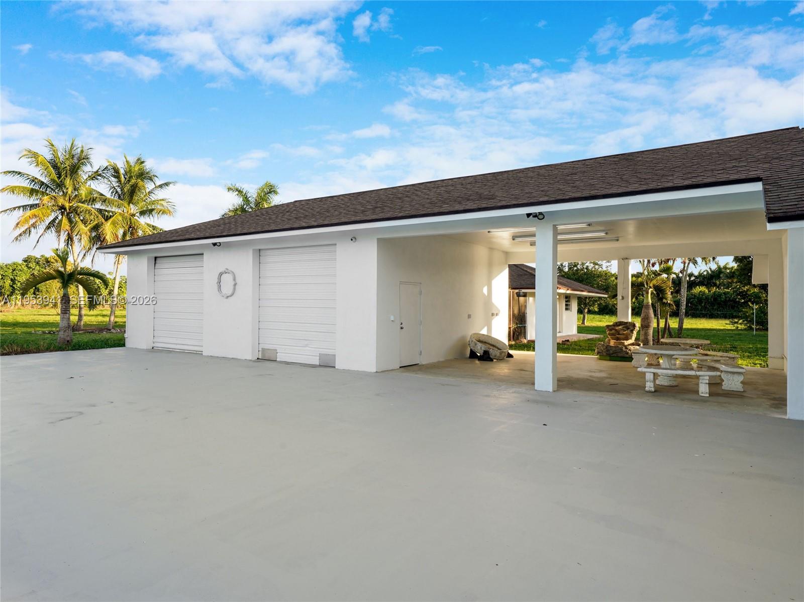 A white building features two garage doors and an open-air carport with a concrete floor — 20000 SW 216th St, Miami FL 33170, MIAMI, FL