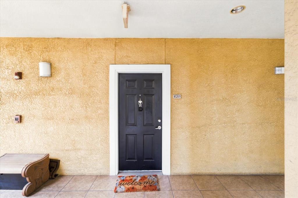 A black front door with a welcome mat is centered on a textured yellow wall — 1910 E PALM AVENUE UNIT 10205, TAMPA, FL
