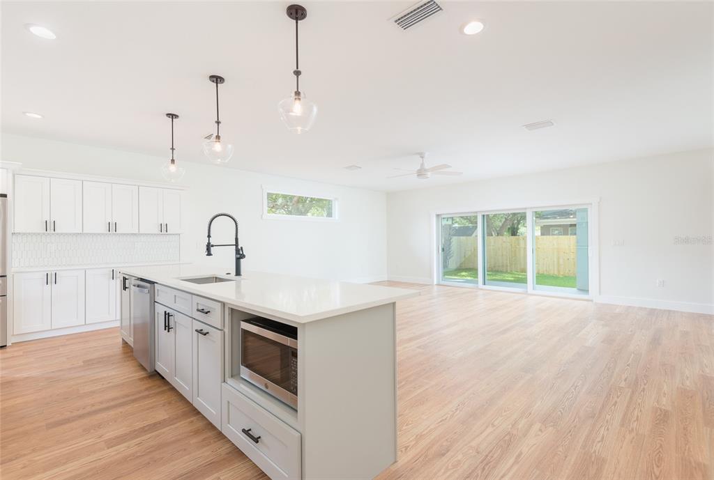 A kitchen with white cabinets, a gray island, and light wood flooring opens to a living area — 3414 W CHEROKEE AVENUE, TAMPA, FL