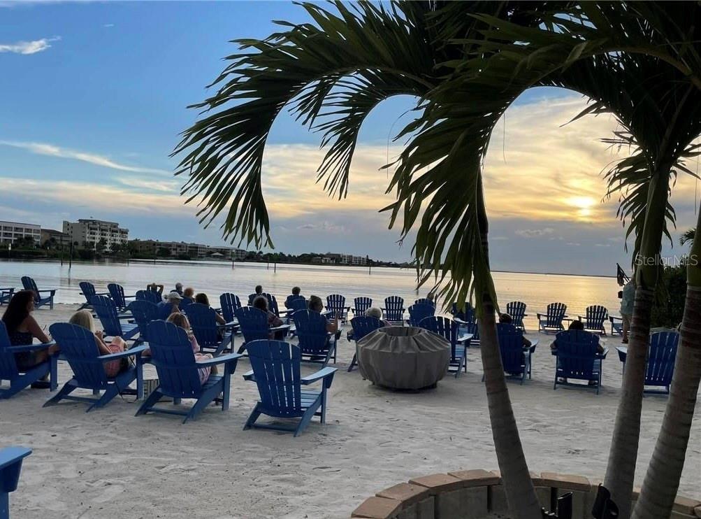 A sandy beach area features numerous blue Adirondack chairs facing a sunset over the water — 27102 CHULA VISTA DRIVE, PUNTA GORDA, FL