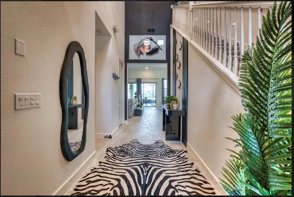 A bright entryway features a zebra-print rug, a tall mirror, and a staircase with white railings — 6301 SAND SKIPPER ROAD, ORLANDO, FL