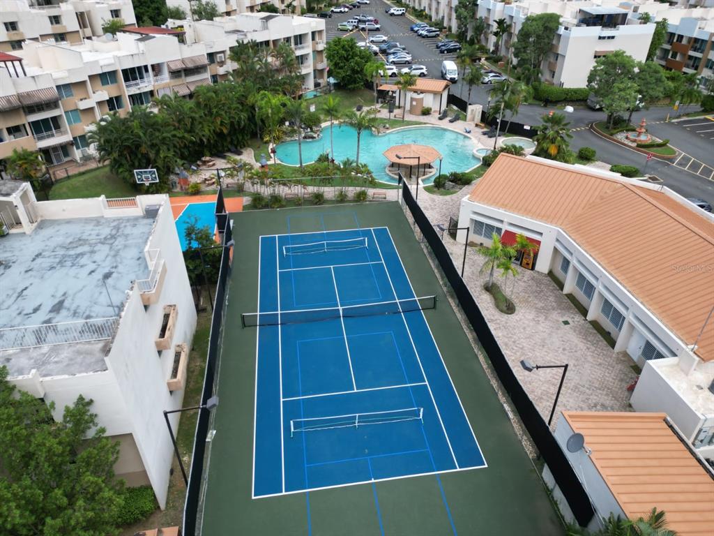 A swimming pool surrounded by palm trees, grass, and residential buildings under a cloudy sky — 109 CALLE PLUMOSO REAL UNIT H104, GUAYNABO, PR