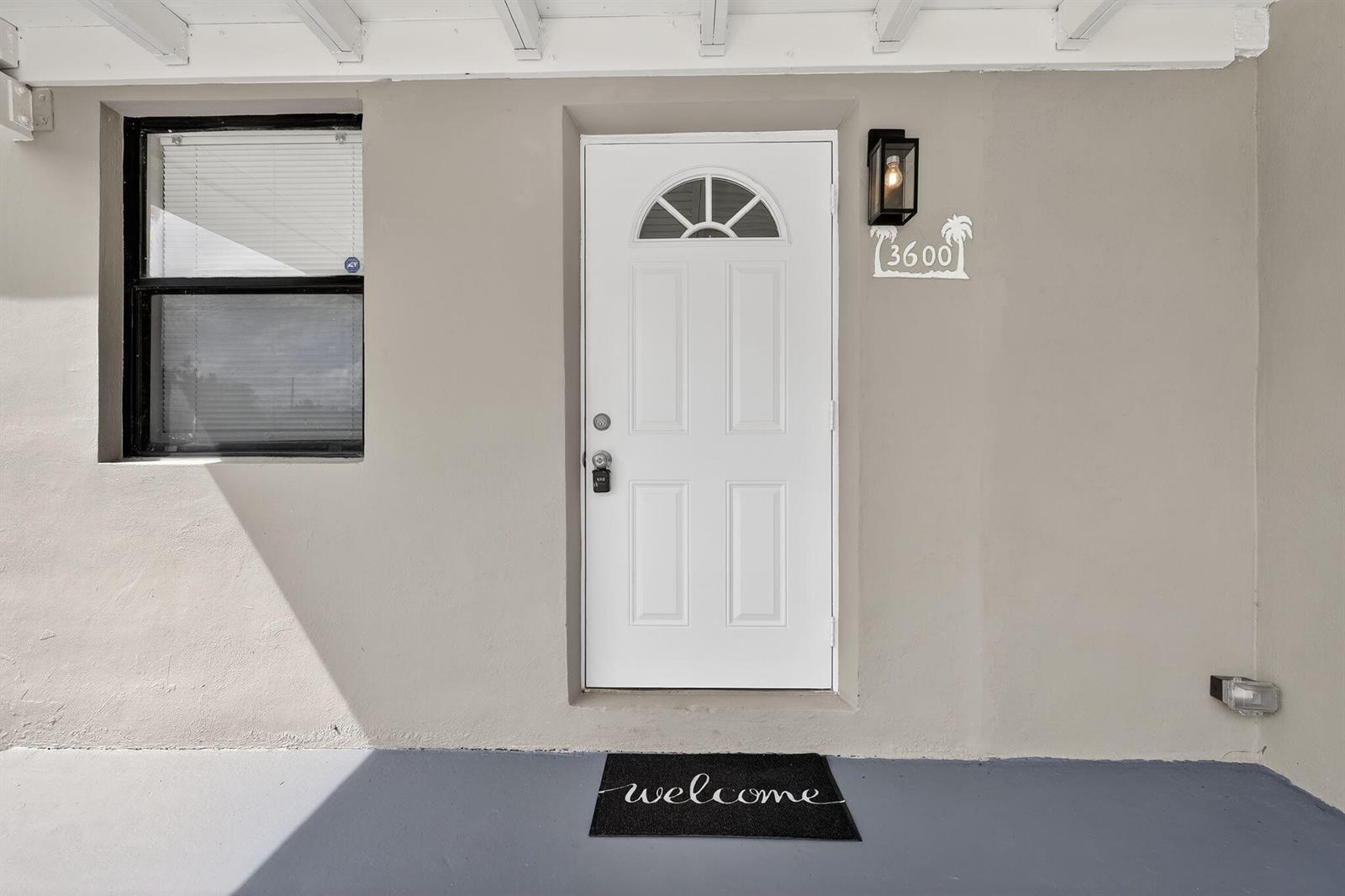 A white front door with a small window sits next to a window and light — 3600 SW 46th Avenue, West Park FL 33023, WEST PARK, FL