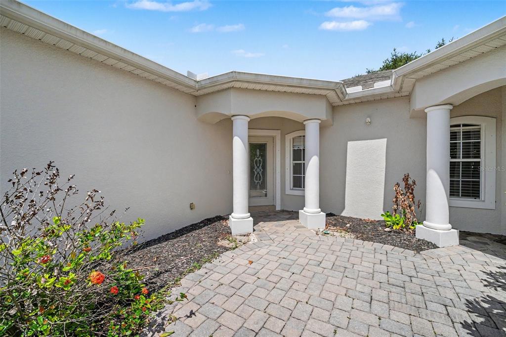 The exterior of a house features a paved walkway leading to a columned entryway — 1819 TULLAGEE AVENUE AVENUE, MELBOURNE, FL