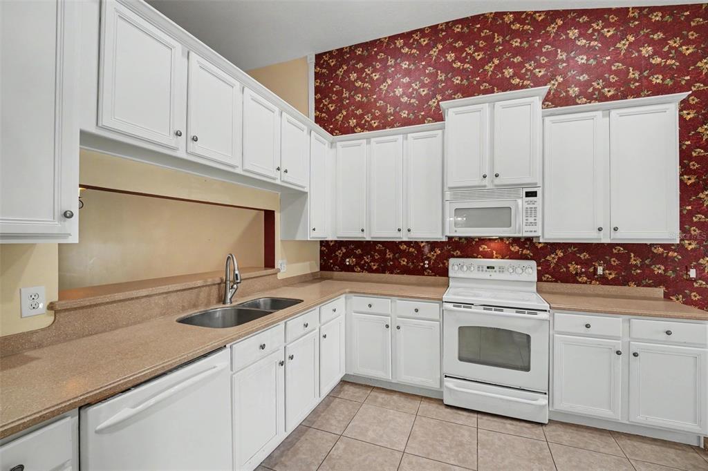 A kitchen features white cabinets, tan countertops, a white stove, and red floral wallpaper — 1819 TULLAGEE AVENUE AVENUE, MELBOURNE, FL