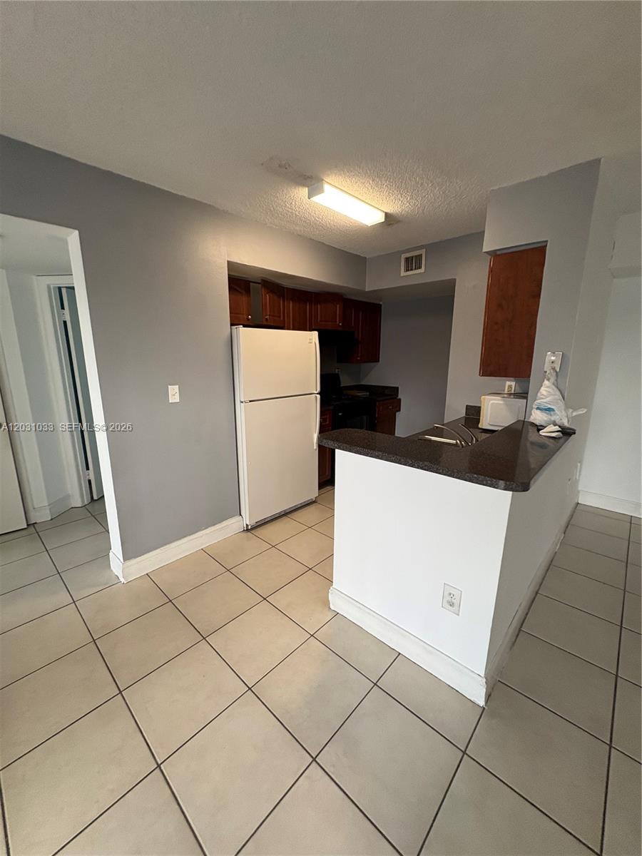 A kitchen features white tile flooring, dark countertops, wooden cabinets, and a white refrigerator — 15231 SW 80th St # 602, Miami FL 33193, MIAMI, FL