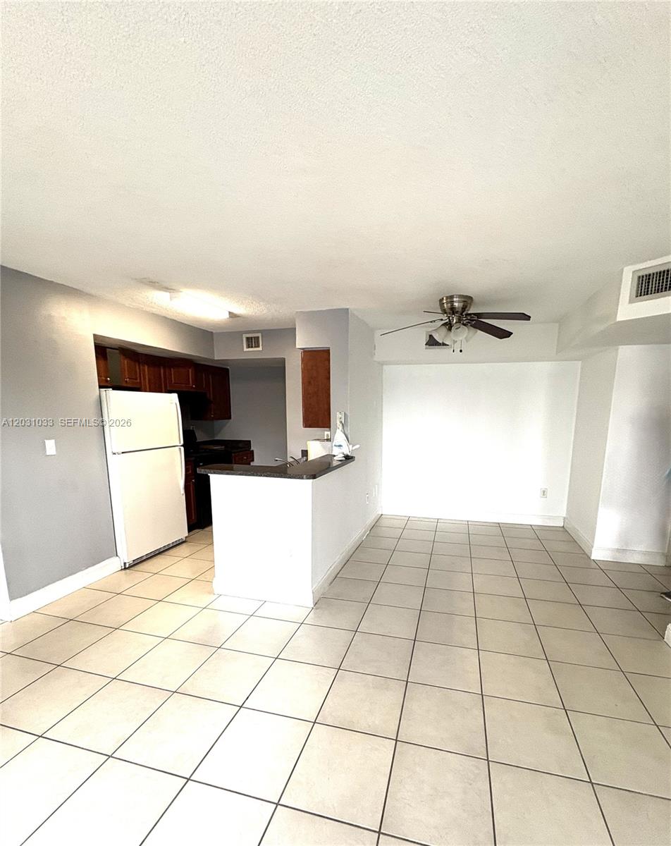 A kitchen with dark wood cabinets and a white refrigerator opens to a tiled dining area — 15231 SW 80th St # 602, Miami FL 33193, MIAMI, FL