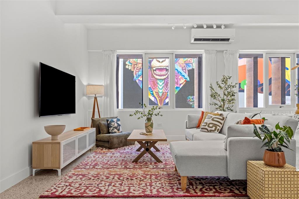 A living room features a sectional sofa, patterned rug, and windows overlooking a colorful mural — 606 CERRA ST, SAN JUAN, PR