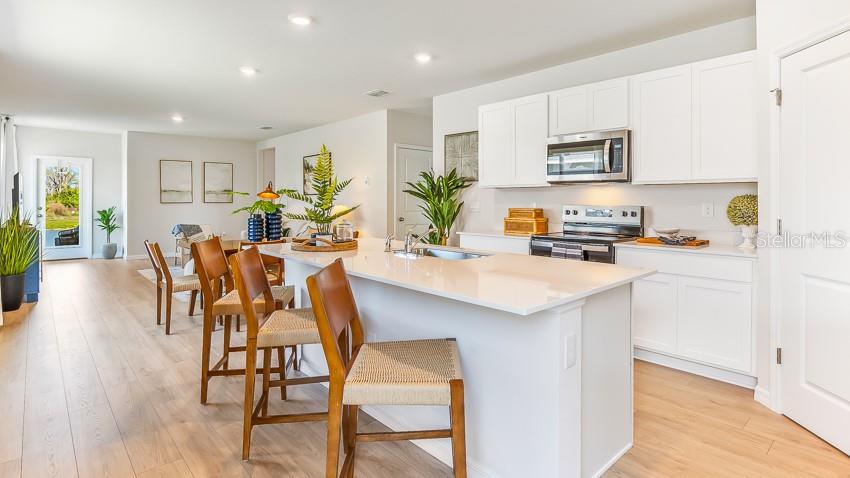 A kitchen with white cabinets and a quartz island overlooks an open-concept living area — 11868 TEXOMA COURT, PARRISH, FL