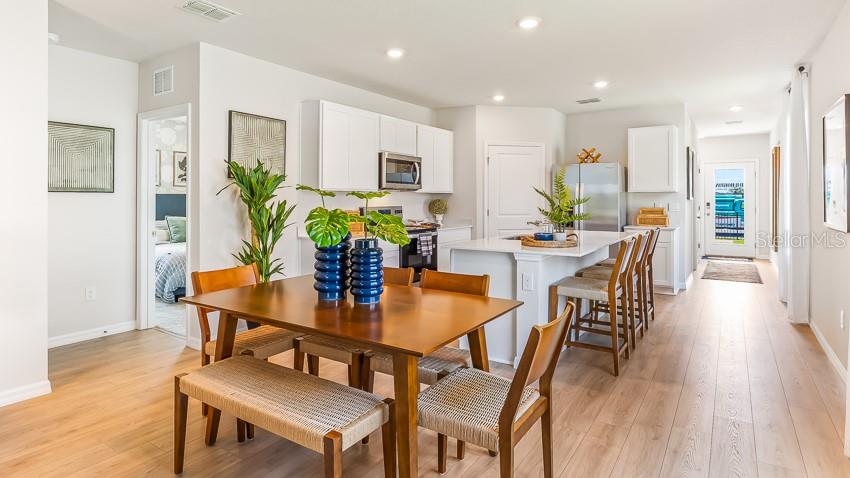 A modern kitchen and dining area feature light wood flooring, white cabinetry, and an island — 11868 TEXOMA COURT, PARRISH, FL