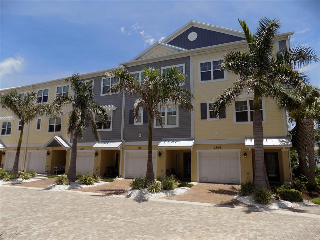 A row of three-story townhomes with yellow and gray siding, garages, and palm trees — 2511 CORAL COURT, INDIAN ROCKS BEACH, FL