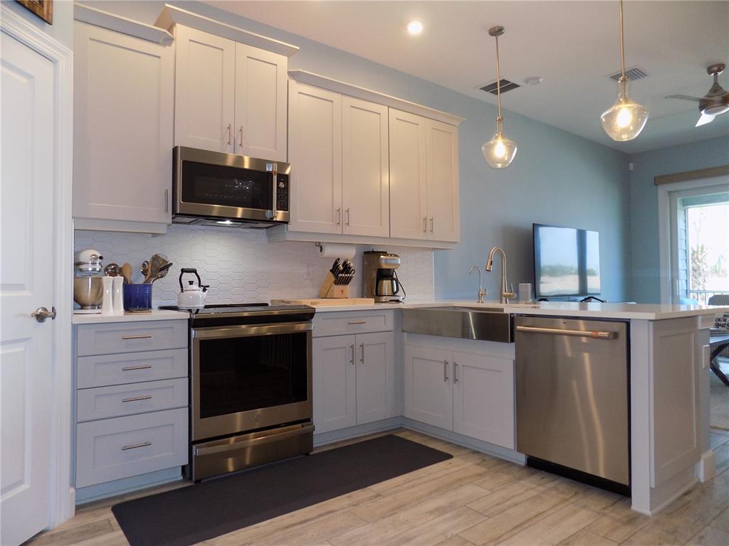 A kitchen features light gray cabinets, stainless steel appliances, a farmhouse sink, and pendant lighting — 2511 CORAL COURT, INDIAN ROCKS BEACH, FL