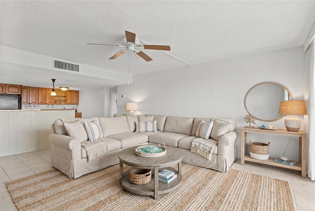A living room features a beige sectional sofa, a round wooden coffee table, and a mirror — 500 TREASURE ISLAND CAUSEWAY UNIT 406, TREASURE ISLAND, FL