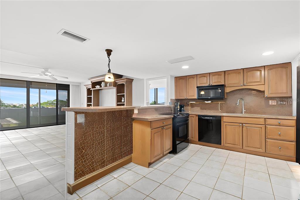 A kitchen with light wood cabinets, black appliances, and a tiled breakfast bar — 500 TREASURE ISLAND CAUSEWAY UNIT 406, TREASURE ISLAND, FL