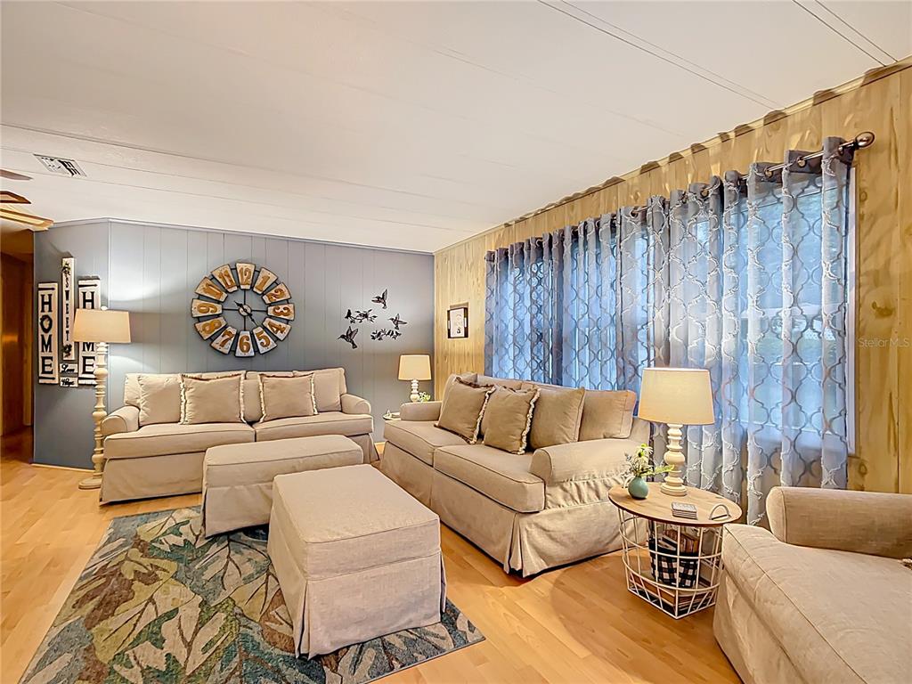 A living room features two beige sofas, a large wall clock, and patterned window curtains — 6044 GRAND OAKS DRIVE SE, WINTER HAVEN, FL